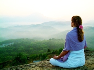 Woman meditating on a misty mountain as sun rises